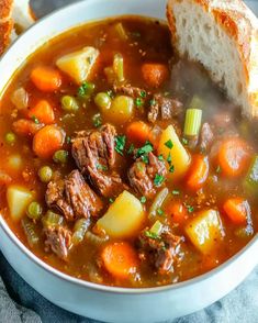 a white bowl filled with beef and vegetable soup on top of a blue towel next to bread