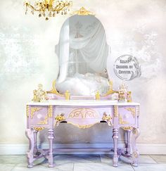 an ornate pink vanity with gold accents in front of a white wall and chandelier