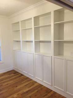 an empty room with white bookcases and wood floors