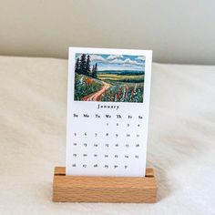 a desk calendar sitting on top of a wooden stand with a landscape painted on it