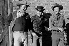 three men standing next to each other in front of a brick wall