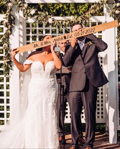 a bride and groom holding up a wooden sign