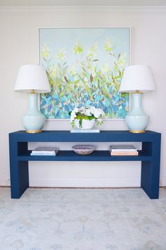 a blue console table with two lamps and a painting on the wall in the background