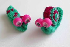 two crocheted green and pink objects on a white table top, one with eyeballs attached to it