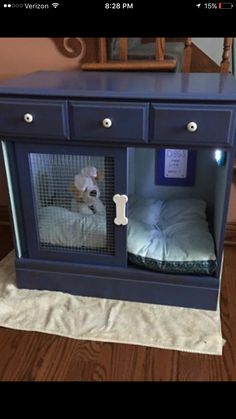 a dog in a cage on top of a wooden table next to a bed with a pillow