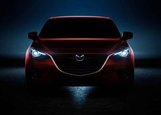 the front end of a red mazda car with its headlights turned on at night time