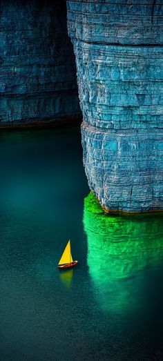 a small boat floating on top of a body of water next to a large cliff