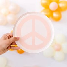 a person holding up a paper plate with a peace sign on it and balloons in the background