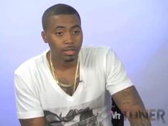 a man sitting down in front of a blue wall wearing a white t - shirt