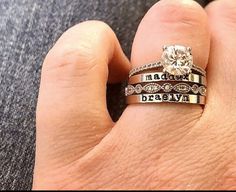 a person's hand holding two wedding rings with names on the band and an engagement ring