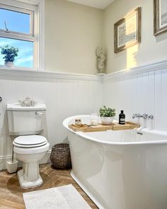 a white bath tub sitting next to a toilet in a bathroom under a window with pictures on the wall