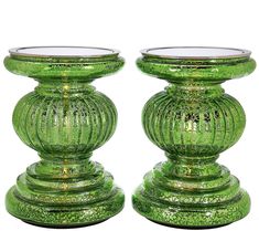 two green glass candlesticks sitting on top of each other in front of a white background