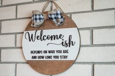 a welcome sign hanging on the side of a brick wall with two bow ties attached to it