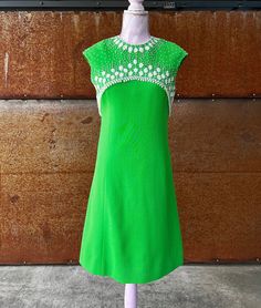 a green dress is on display in front of a wooden wall with a white beaded neckline