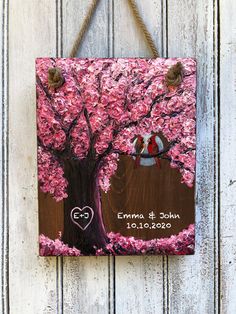 a wooden sign hanging on the side of a white wall with pink flowers and two birds in a tree