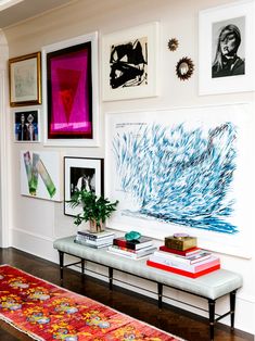 a living room filled with lots of art on the wall above a white bench next to a rug