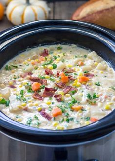 a crock pot filled with corn, bacon and carrots next to some bread