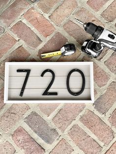 a house number sign sitting on top of a brick floor next to two drillers