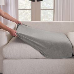 a person is unpacking a gray blanket on a white couch in front of a window