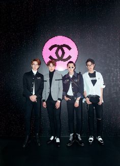 four young men standing in front of a chanel logo on a black wall with pink dots