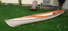 a wooden canoe sitting on the grass in front of a house with a lawn chair next to it