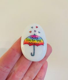 a hand holding a white button with an umbrella painted on it's front and back