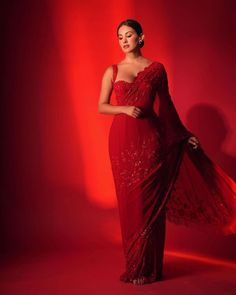 a woman in a red sari poses for a photo with her hands on her hips