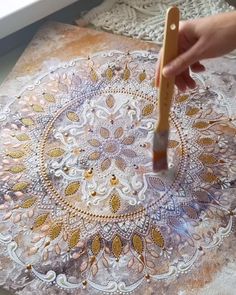 a person using a brush to paint an ornate doily