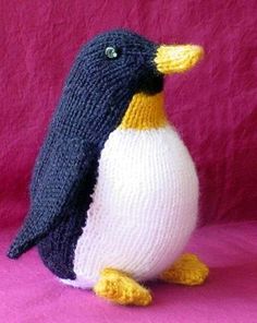 a knitted penguin sitting on top of a pink blanket next to a purple wall