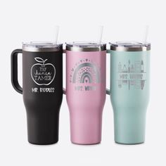 three different colored travel mugs with lids and straws in each cup, one has an apple on it