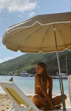 a woman sitting on the beach under an umbrella