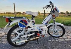 a white and blue motorcycle parked on top of a cobblestone road next to a field