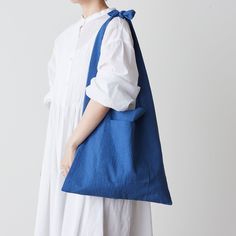 a woman in white dress carrying a blue tote bag with an attached shoulder strap