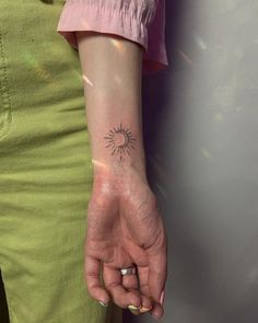 a woman's arm with a small sun tattoo on her left hand and a ring in the middle