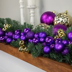 purple and gold ornaments are sitting on the mantle in front of a christmas garland with pine branches