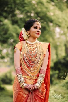 a woman in an orange and gold outfit with jewelry on her neck, standing outside