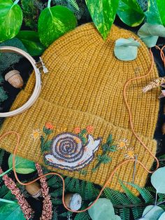 a knitted hat is surrounded by green leaves and other foliage, including an acorn