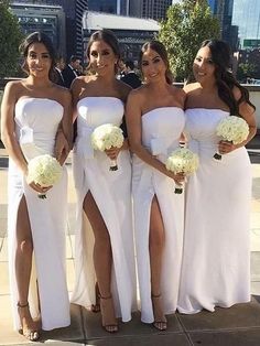 four bridesmaids in white dresses posing for the camera with their bouquets on