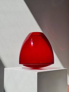 a red vase sitting on top of a white block next to a shadow filled wall