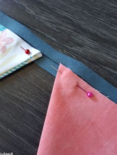 two pieces of fabric are laying next to each other on a table with sewing needles