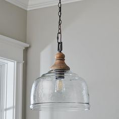 a clear glass light fixture hanging from a ceiling in a room with white walls and windows