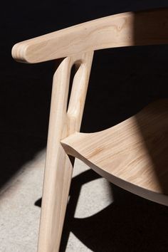 a wooden chair sitting on top of a white floor next to a black wall with light coming through it