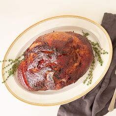 a cooked meat on a white plate with herbs and silverware next to the dish