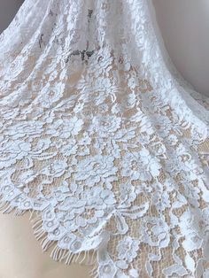 a white lace fabric with flowers and leaves on the bottom is shown in full view