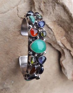 "The handmade cuff bracelet is made with 18 natural colorful gemstones. The center gem is aqua chalcedony, the others are amethyst, peridot, amber, blue topaz with one smaller onyx stone. The gemstones are set in a smooth bezel with Navajo pearl beads accented around each stone. The cuff bracelet is well made, condition is excellent and the cuff has substantial weight of 54.4 grams. The gemstone cuff is Sterling silver. Handmade by Bea Tom Native American. Bea Tom is affiliated with the Navajo t Fusion Style Cuff Bracelet With Natural Stones, Artisan Gemstone Bangle Jewelry, Unique Multi-stone Bracelet, Fusion Style Gemstone Cuff Bracelet, Unique Multi-stone Bracelet Jewelry, Multicolor Gemstone Cuff Bracelet As Gift, Fusion Style Multi-stone Bangle Jewelry, Unique Multi-stone Bangle Jewelry, Multi-stone Fusion Bracelet