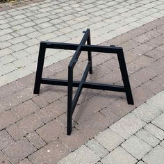 a black metal object sitting on top of a brick walkway next to a sidewalk with cobblestone