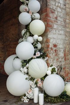 white balloons and greenery are arranged on the floor in front of a brick wall