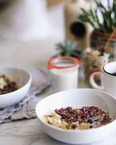 two white bowls filled with food sitting on top of a table next to coffee cups