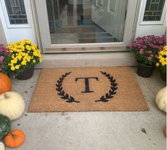 a door mat with the letter t on it in front of flowers and pumpkins