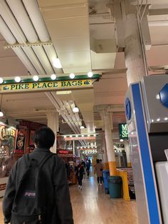 a man is walking through the store with his back to the camera and there are many signs on the ceiling above him